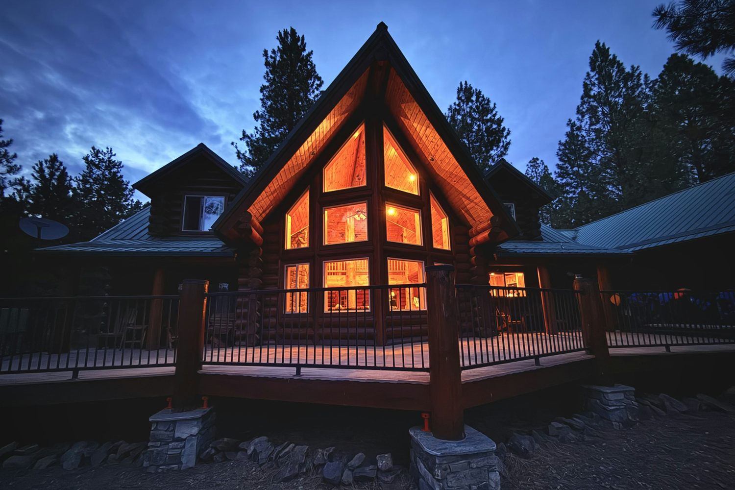 Log mountain home with a wraparound deck at dusk